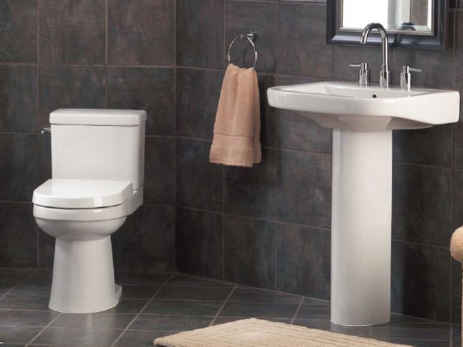 BAthroom with dark gret tile walls and white toilet and pedistal sink
