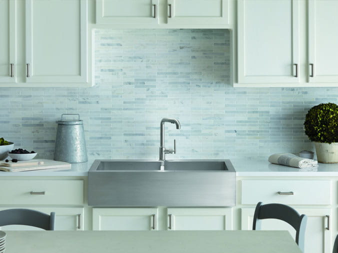 Kohlet farmhouse sink in kitchen with white cabinets and tile backsplash